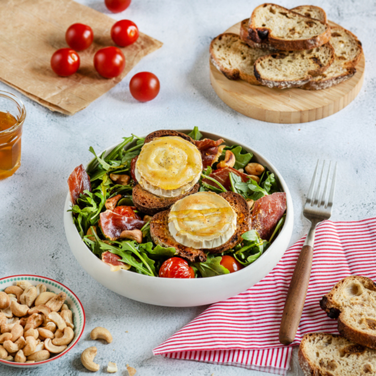 Gourmet salad of warm goat cheese, tomatoes, arugula and cured ham